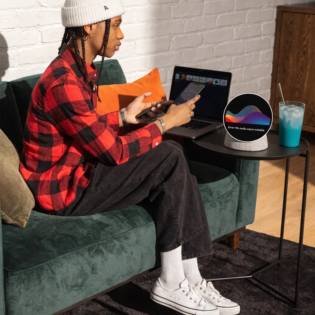 A person troubleshooting Google Home playback issues on a Nest Hub device with a laptop and smartphone in a modern living room.