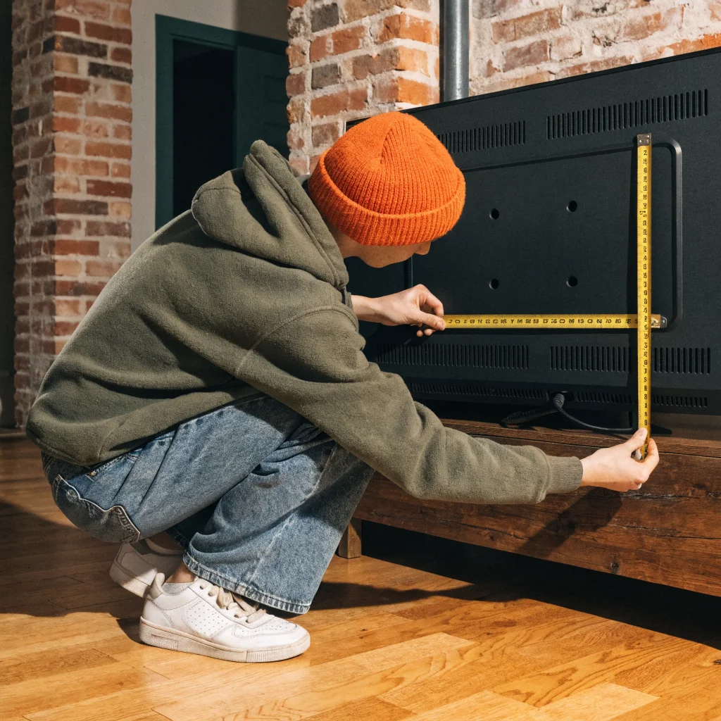 A person measuring the VESA mount holes on the back of a television to ensure compatibility with a 400x400 TV wall mount.