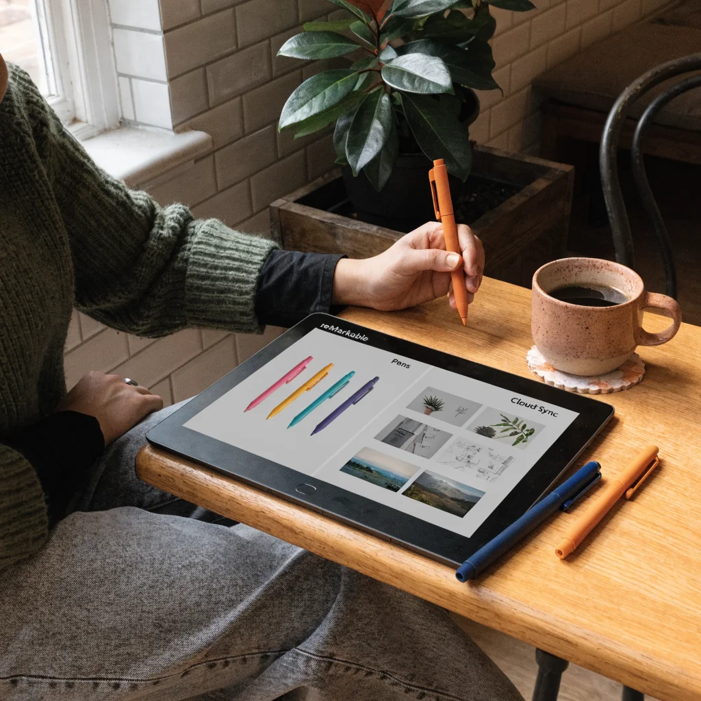 A realistic photo of a reMarkable E-Ink tablet displaying updated software features with colorful pen options and cloud-synced images on the screen.