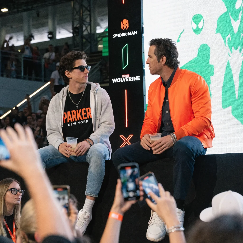 A realistic photo showing actors Peter Parker and Wade Wilson together at a gaming event promoting Insomniac's Spider-Man and Marvel's Wolverine video games.