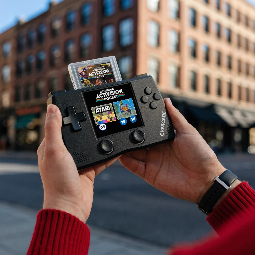 A realistic photo of the Evercade handheld console displaying the Activision Super Pocket cartridge with classic 1980s Atari and 3D platformer games like Banjo-Kazooie on screen.
