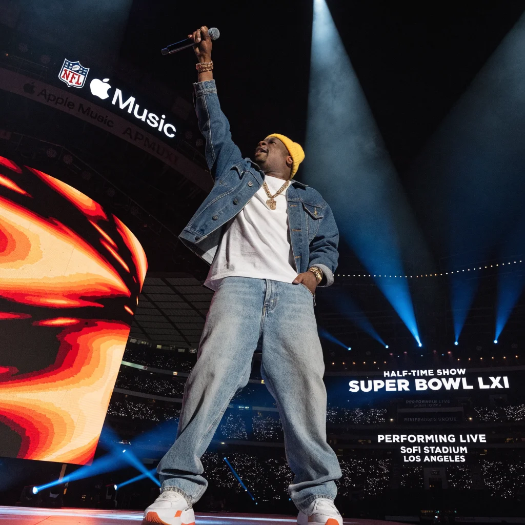 Jay-Z performing live at the Apple Music Half-Time Show during Super Bowl LXI at SoFi Stadium in Los Angeles with NFL and Apple branding visible.