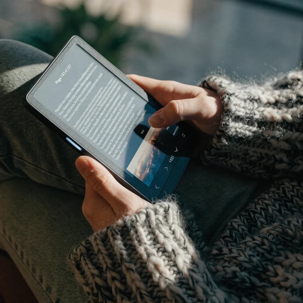 A close-up photo of an Amazon Kindle 2026 showing uneven brightness and screen shadows while reading in dark mode, highlighting the device’s light design and protective glass.