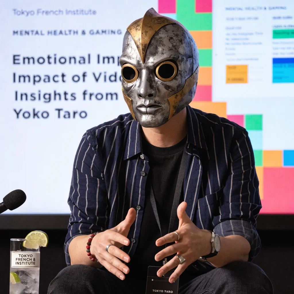 Portrait of Yoko Taro, Japanese game designer known for Nier and Drakengard, wearing Emil mask while speaking at Tokyo French Institute about mental health and gaming.