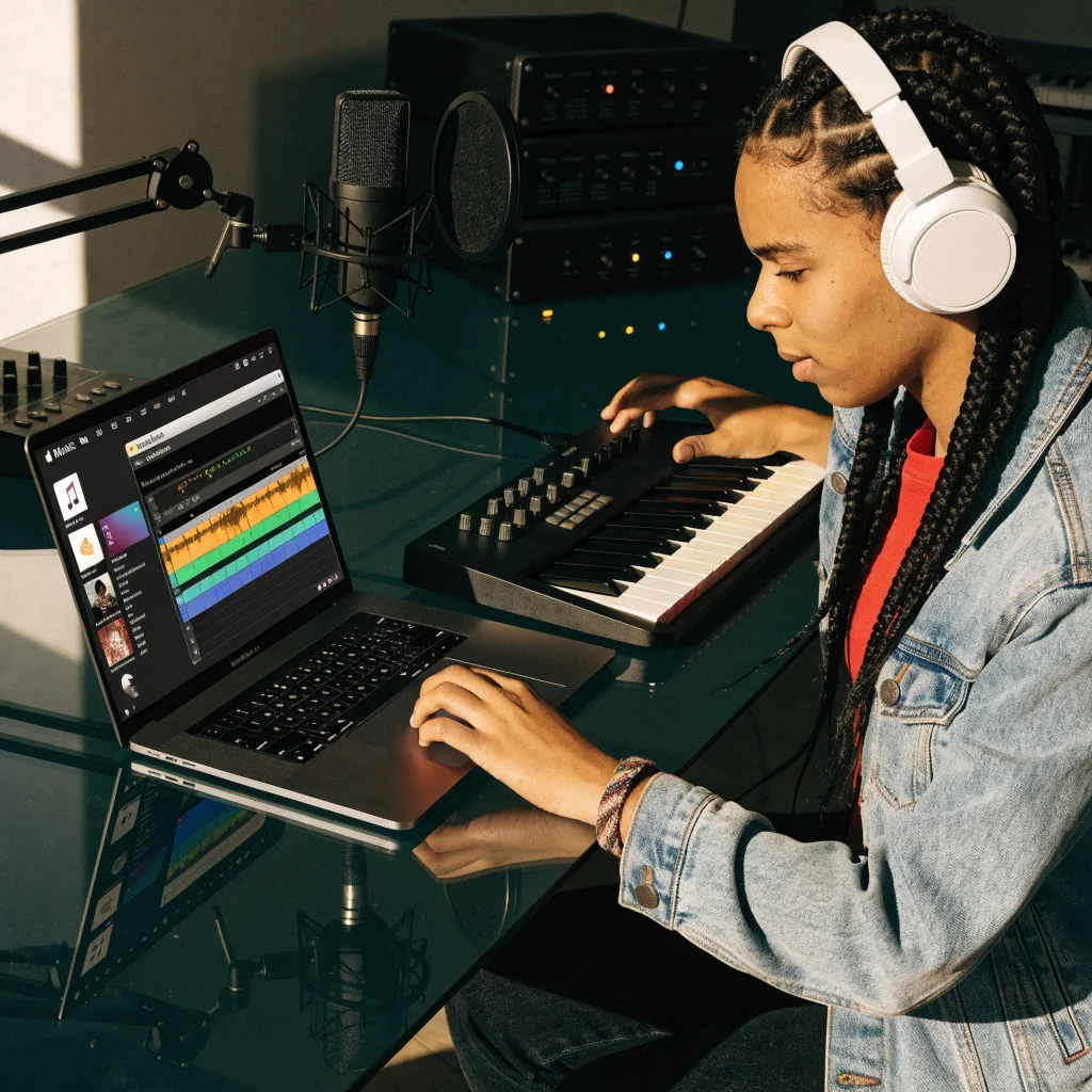 A beginner musician using GarageBand on a MacBook Pro with macOS, creating music in a digital studio environment with Apple Music app visible.
